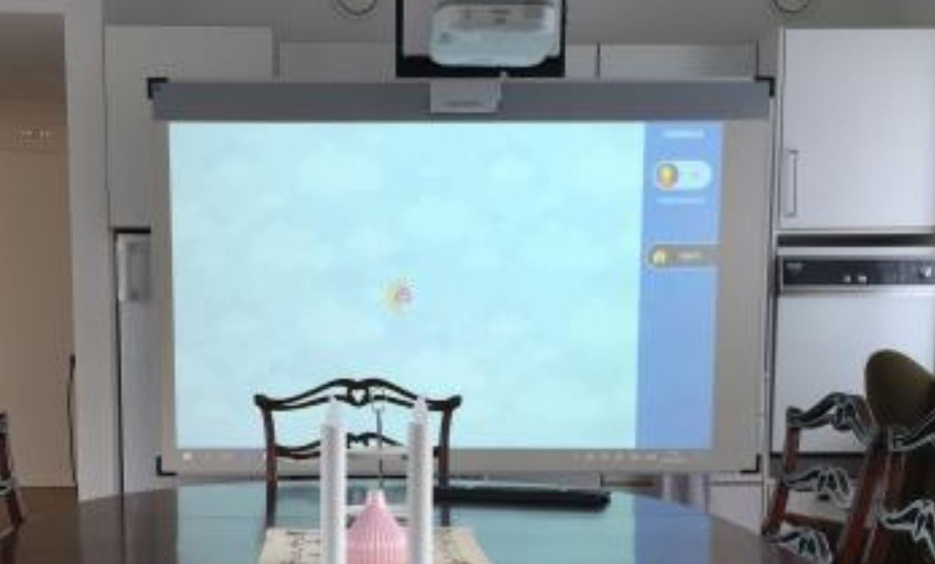 Touch and play skærm i brug. Et lærred er rullet ud - lodret - for enden af et bord og en fremviser hænger i loftet og sender et billede over på lærredet.